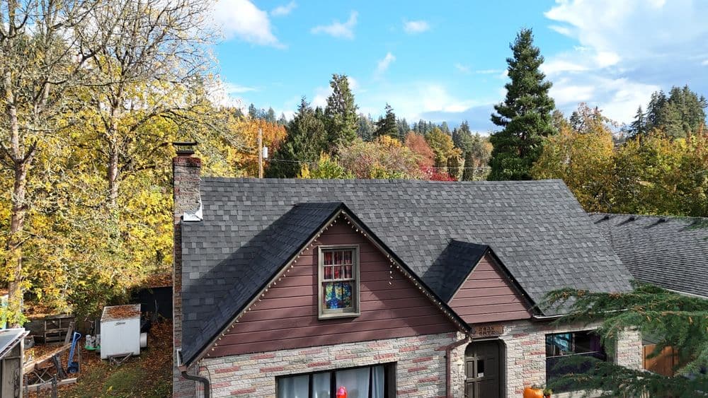Aerial view of a cozy home with a grey roof surrounded by colorful autumn trees.