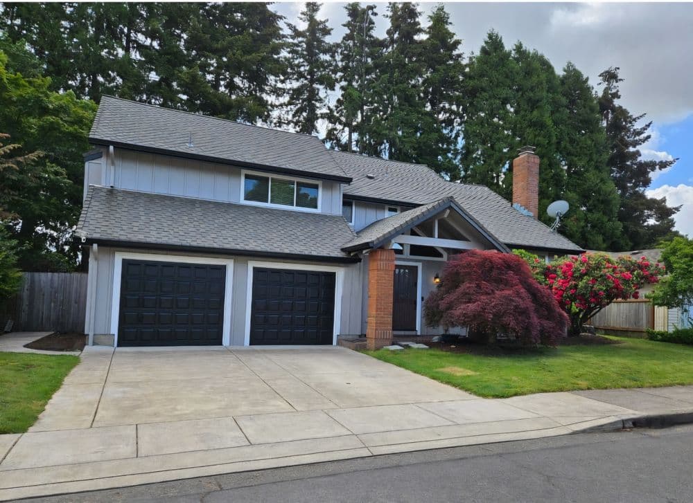 Modern two-story home with a driveway, green lawn, and vibrant landscaping.