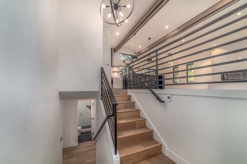 Modern staircase with wooden steps, sleek railing, and contemporary lighting in bright interior.