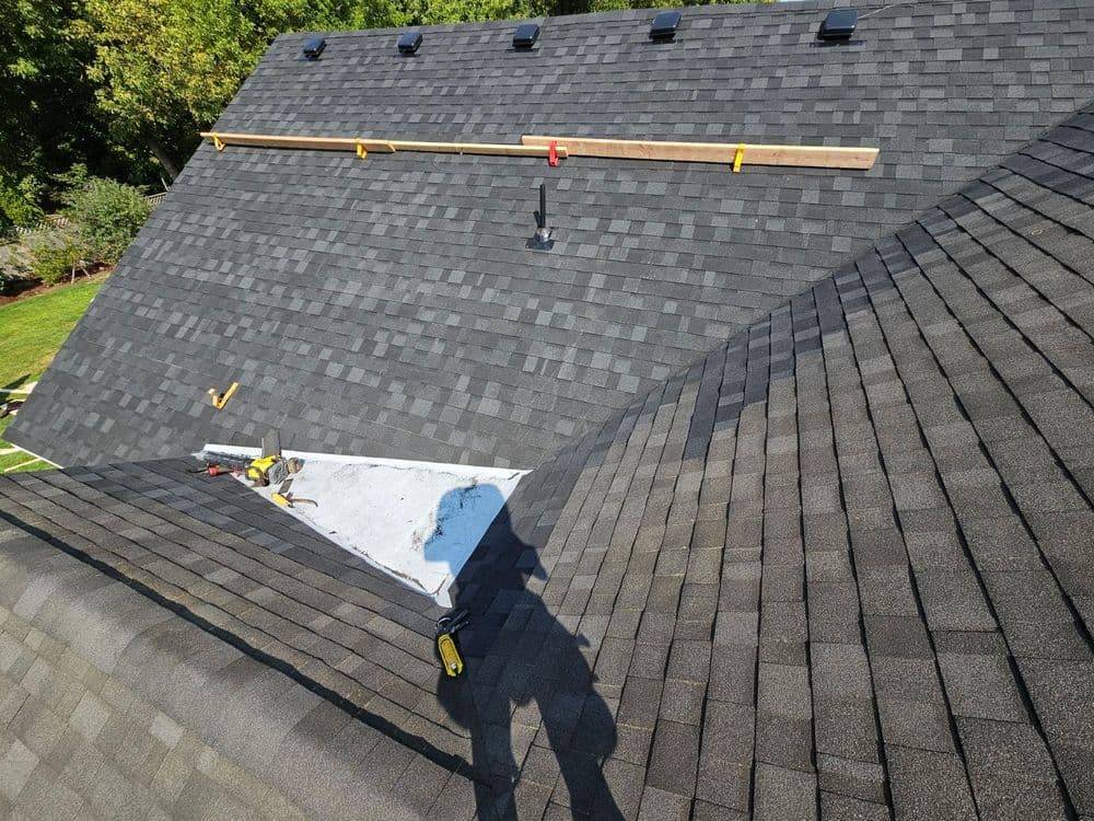 Roofing installation process with shingles, tools and wooden scaffolding visible on sloped surfaces.