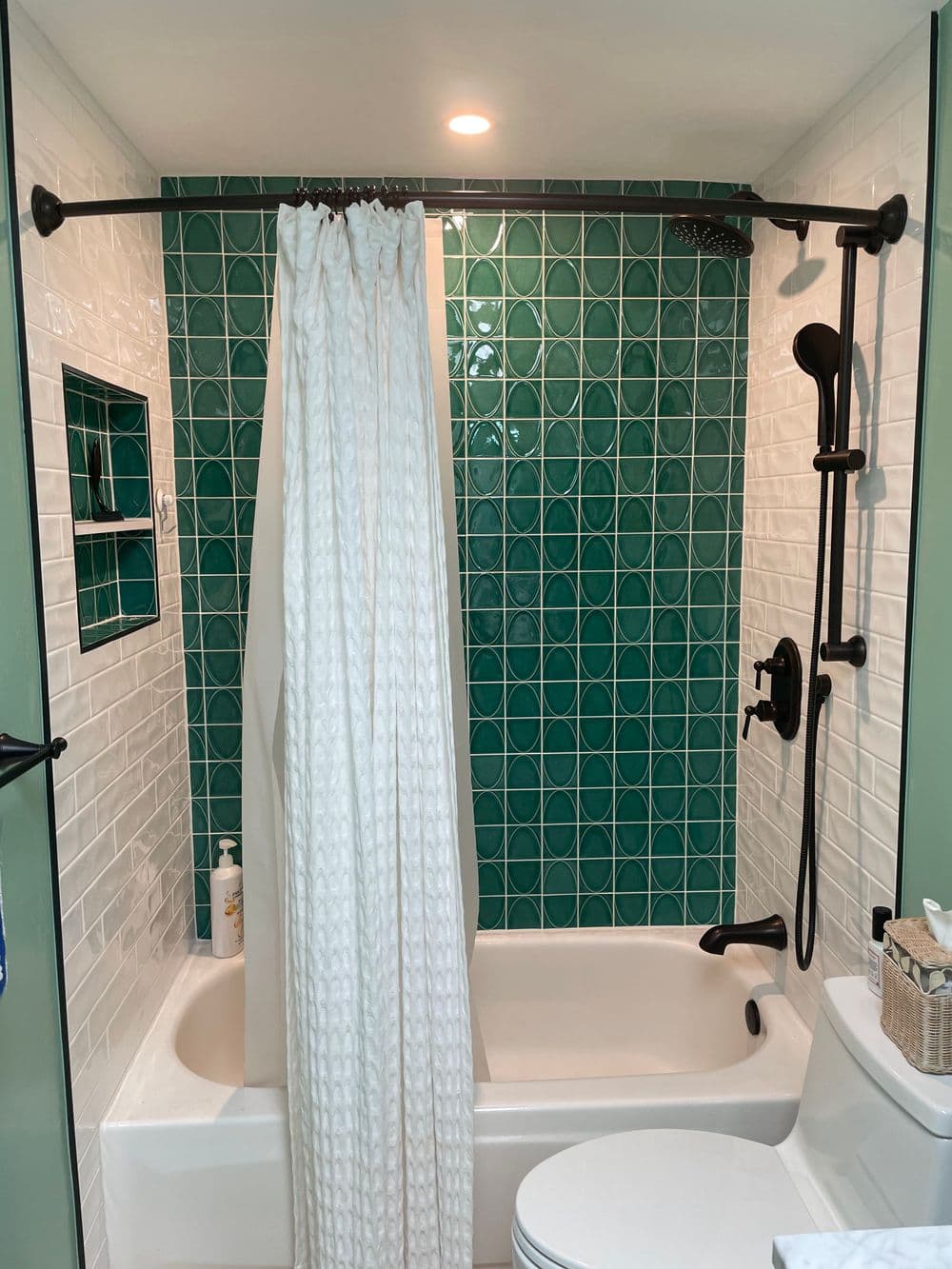 Modern bathroom with teal tiled wall, white shower curtain, and stylish fixtures.