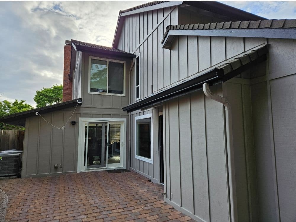 Modern house exterior with gray siding, large windows, and a brick patio.