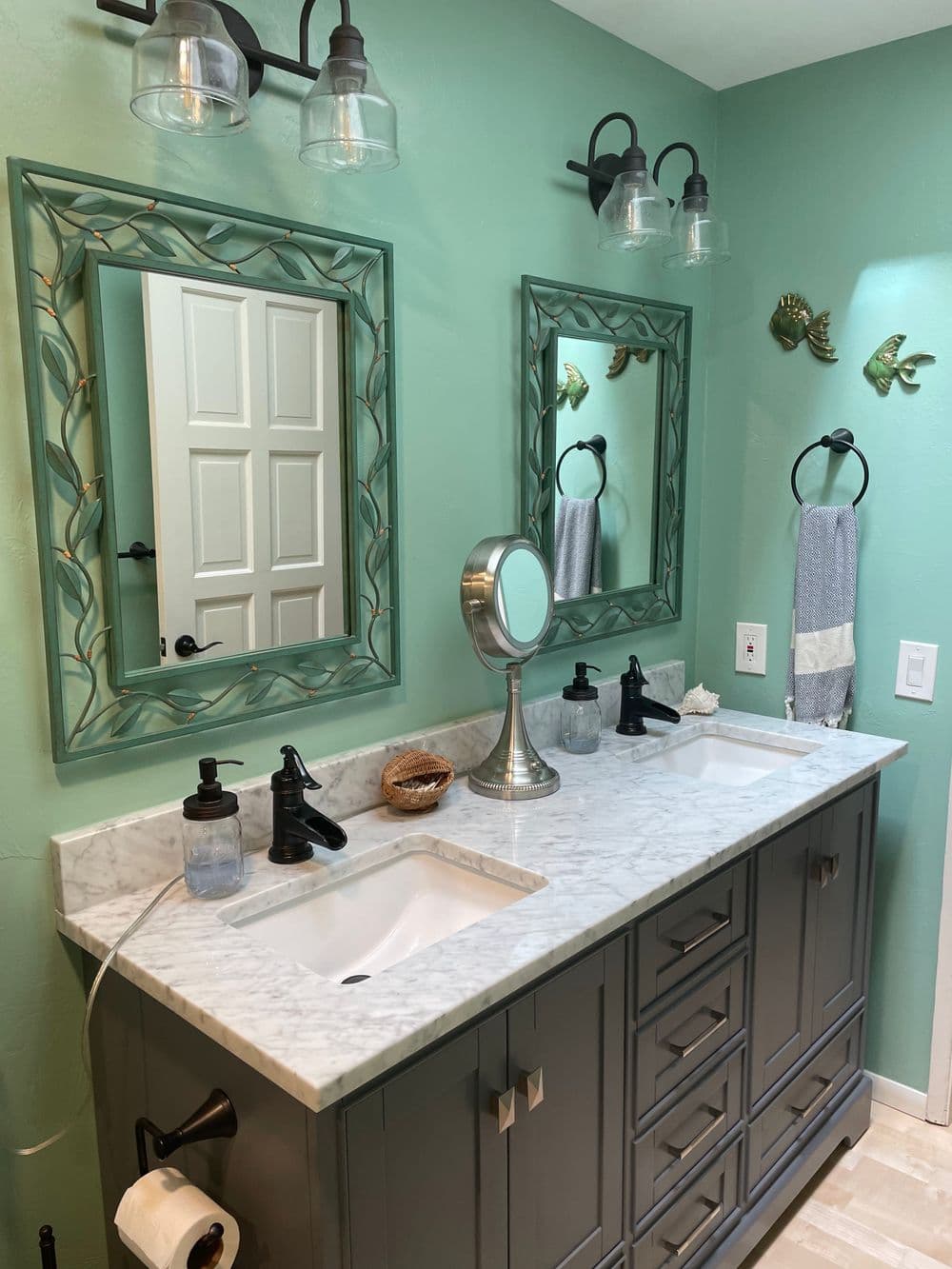 Modern bathroom with dual sinks, marble countertop, teal walls, and decorative mirrors.