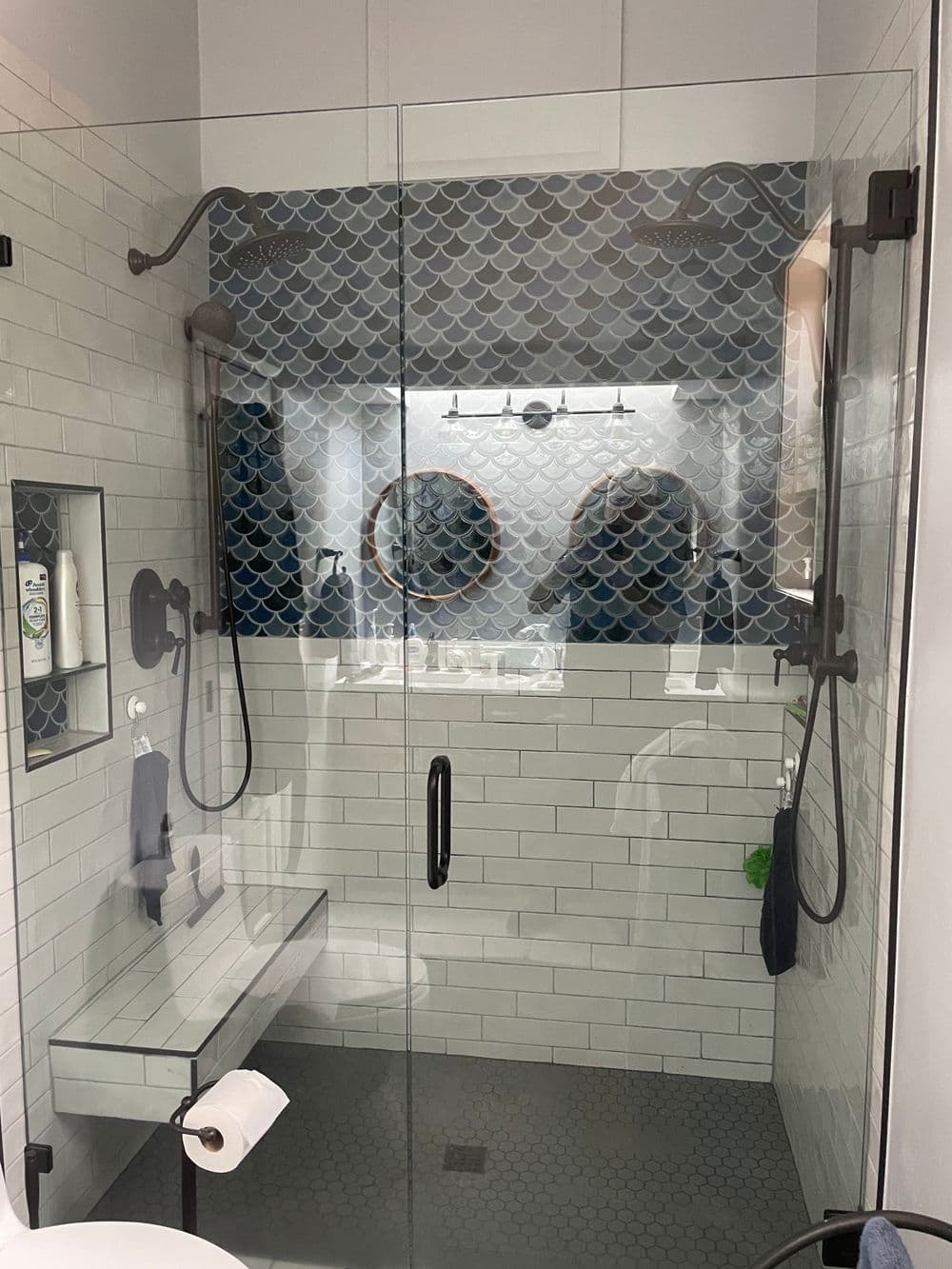 Modern shower design with hexagonal tile, dual showerheads, and glass enclosure featuring blue pattern.
