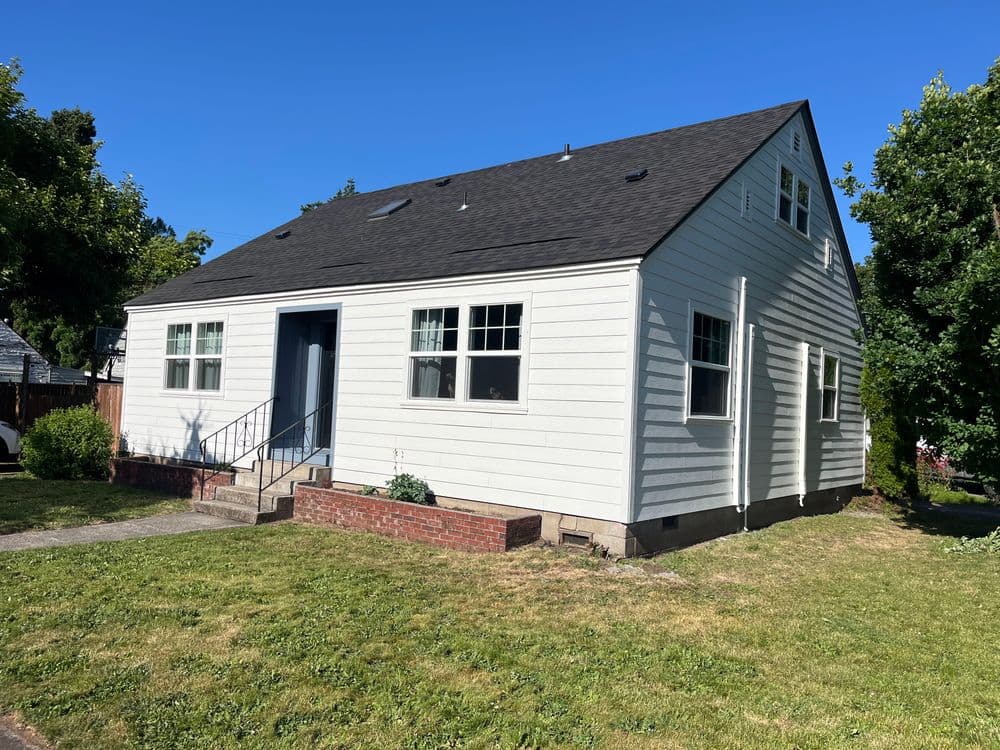 White single-story house with a blue door and grassy lawn under a clear blue sky.
