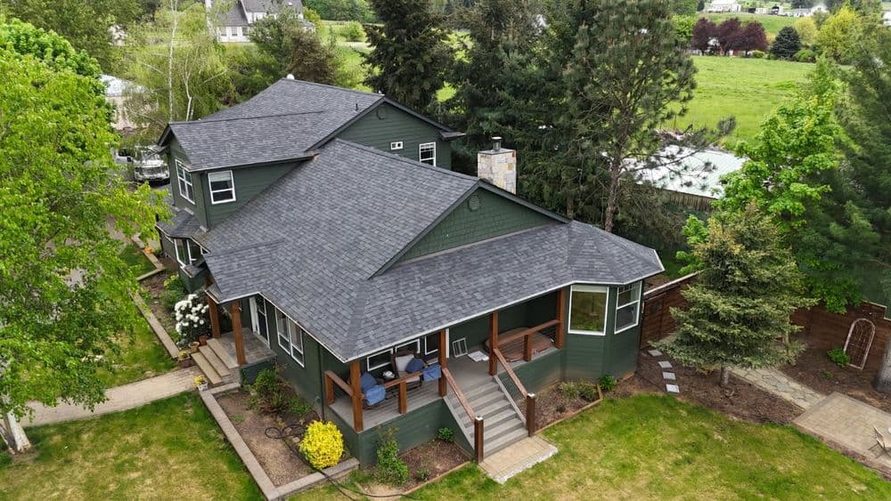 Aerial view of a green house with a large yard and patio area surrounded by trees.