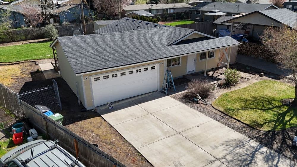 Aerial view of a modern home with a gray roof, driveway, and surrounding yard.
