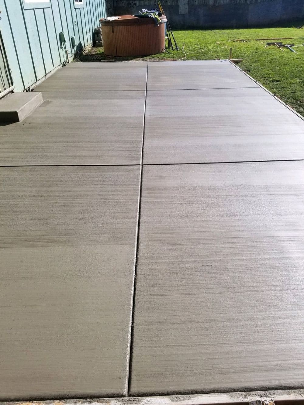 Freshly poured concrete patio with visible texture, adjacent to a wooden hot tub.