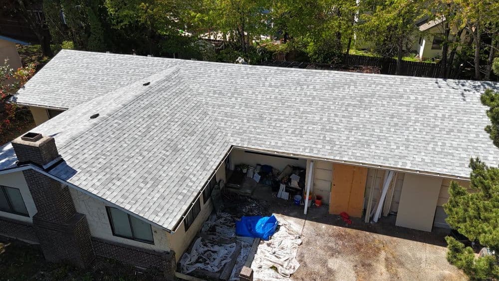 Aerial view of a house with a new gray shingle roof and partially constructed garage.