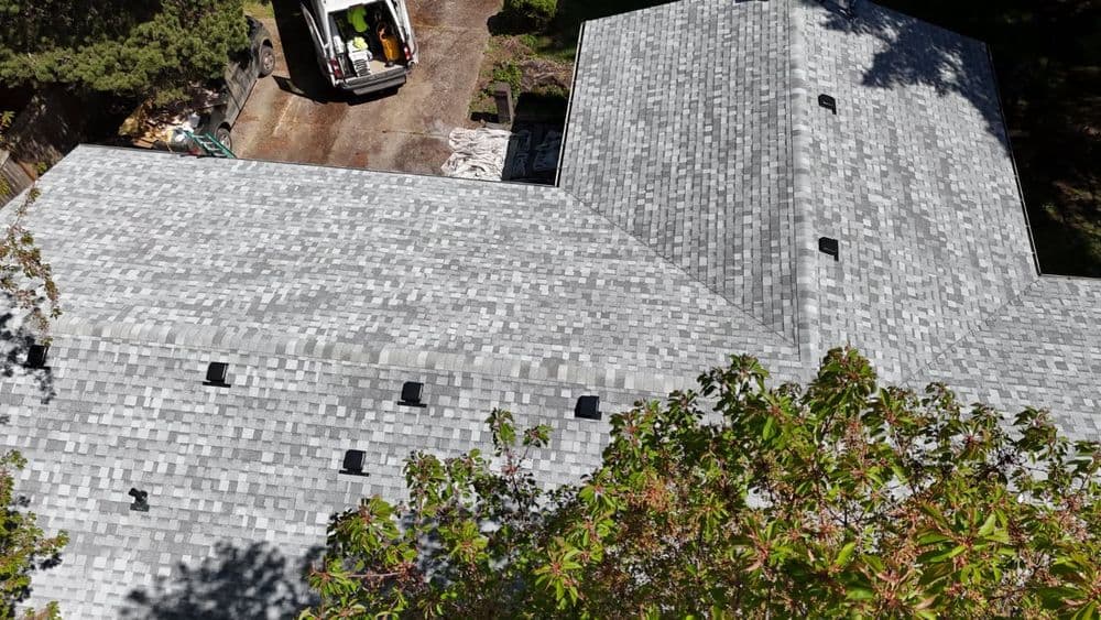 Aerial view of a house with a gray shingle roof and a work vehicle nearby.