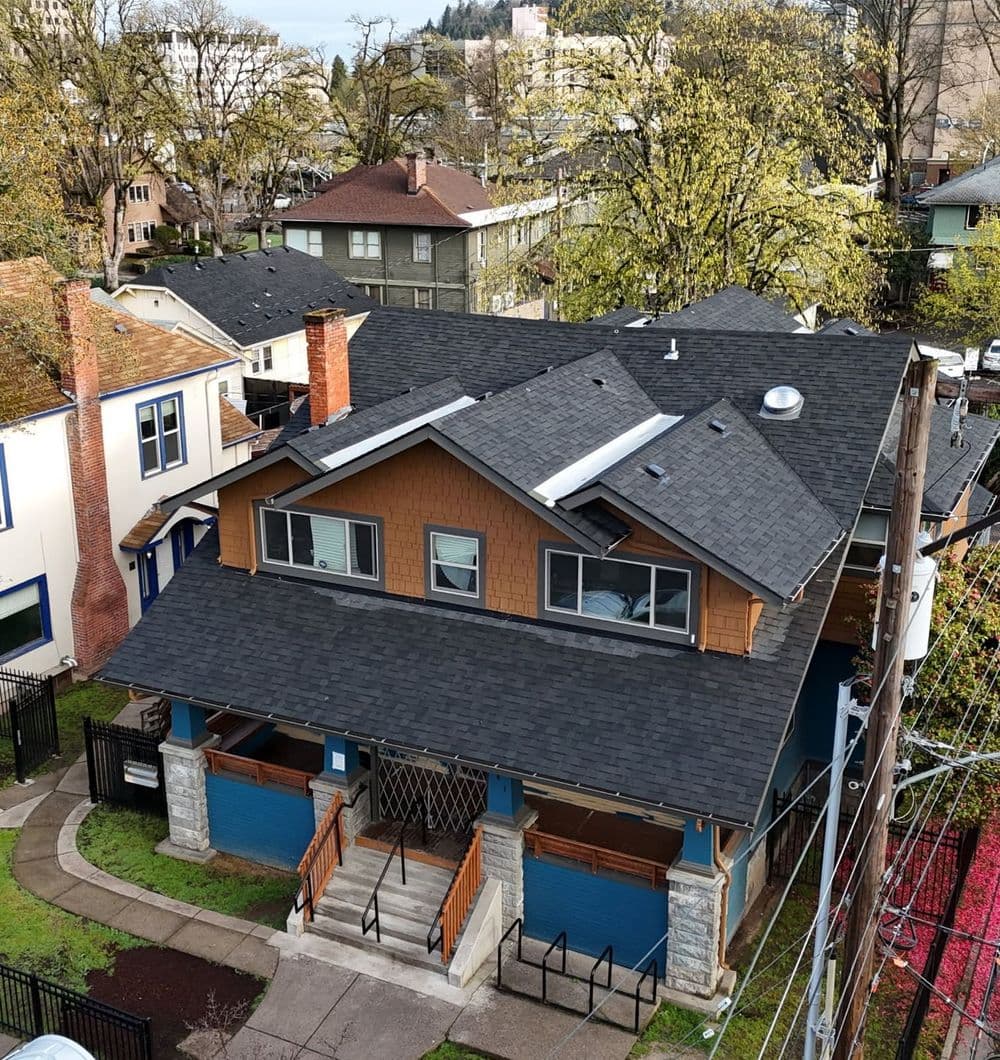 Aerial view of a residential building with a blue exterior and wooden accents in a neighborhood.
