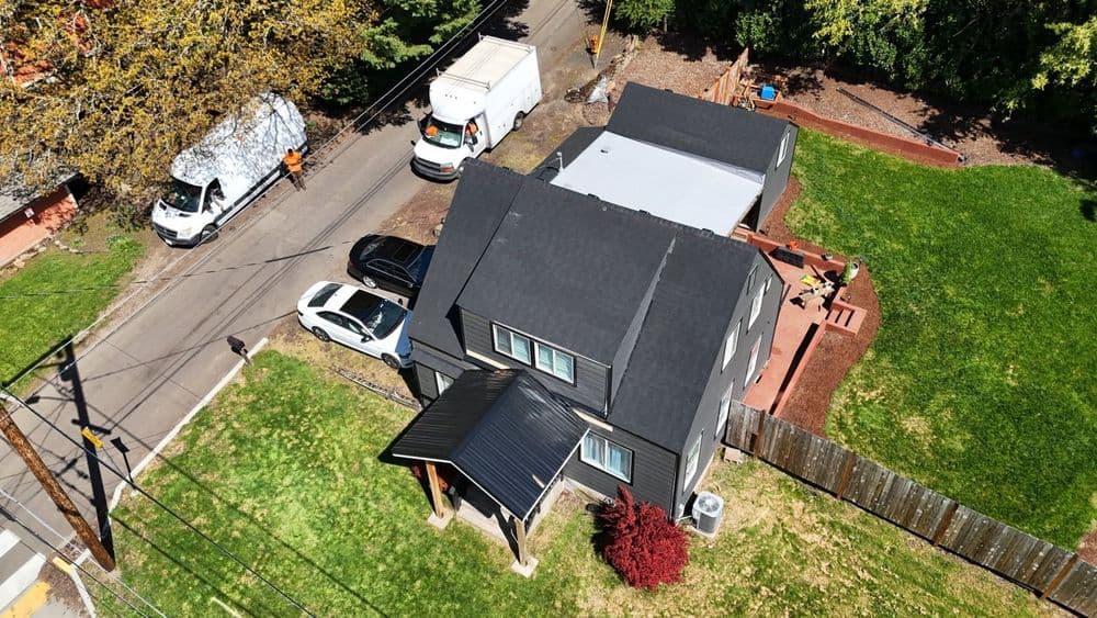 Aerial view of a modern two-story house with a green lawn and parked vehicles nearby.