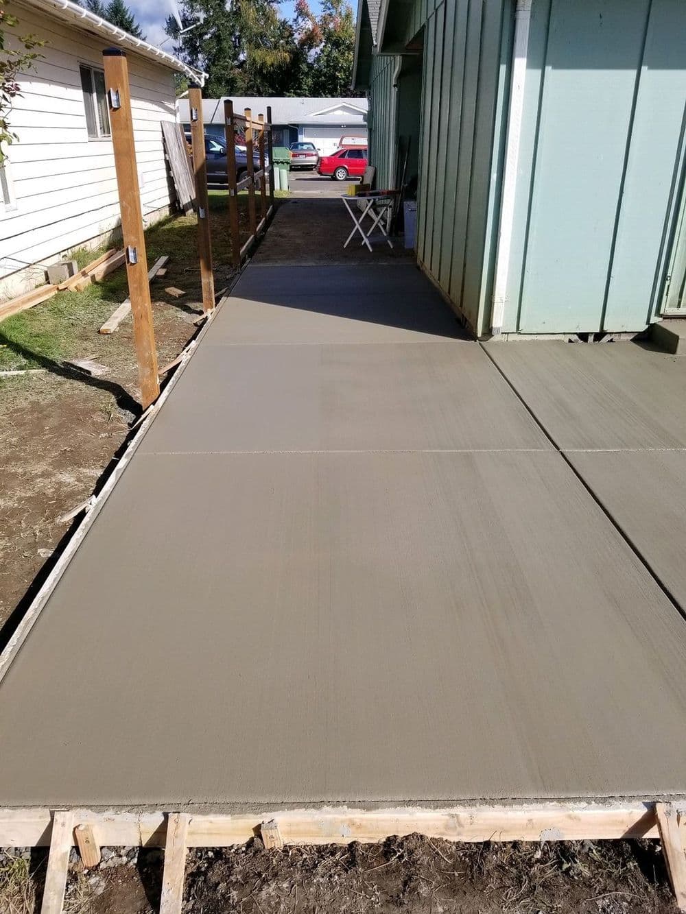Freshly poured concrete sidewalk next to a house and wooden posts, showcasing a construction project.